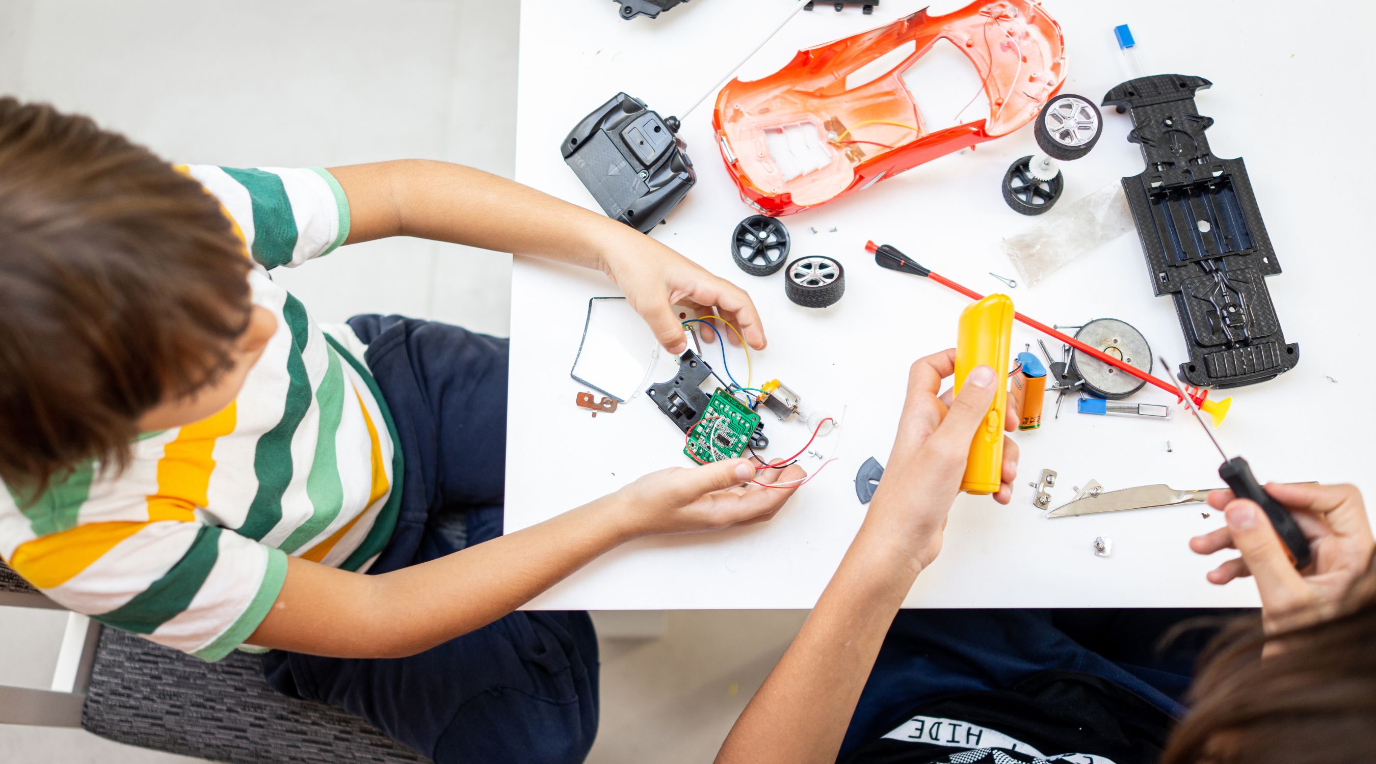 Club de robotique pour jeunes à la MJC de Gex, vue de dessus d'enfants assemblant les composants électroniques et le châssis d'un véhicule miniature