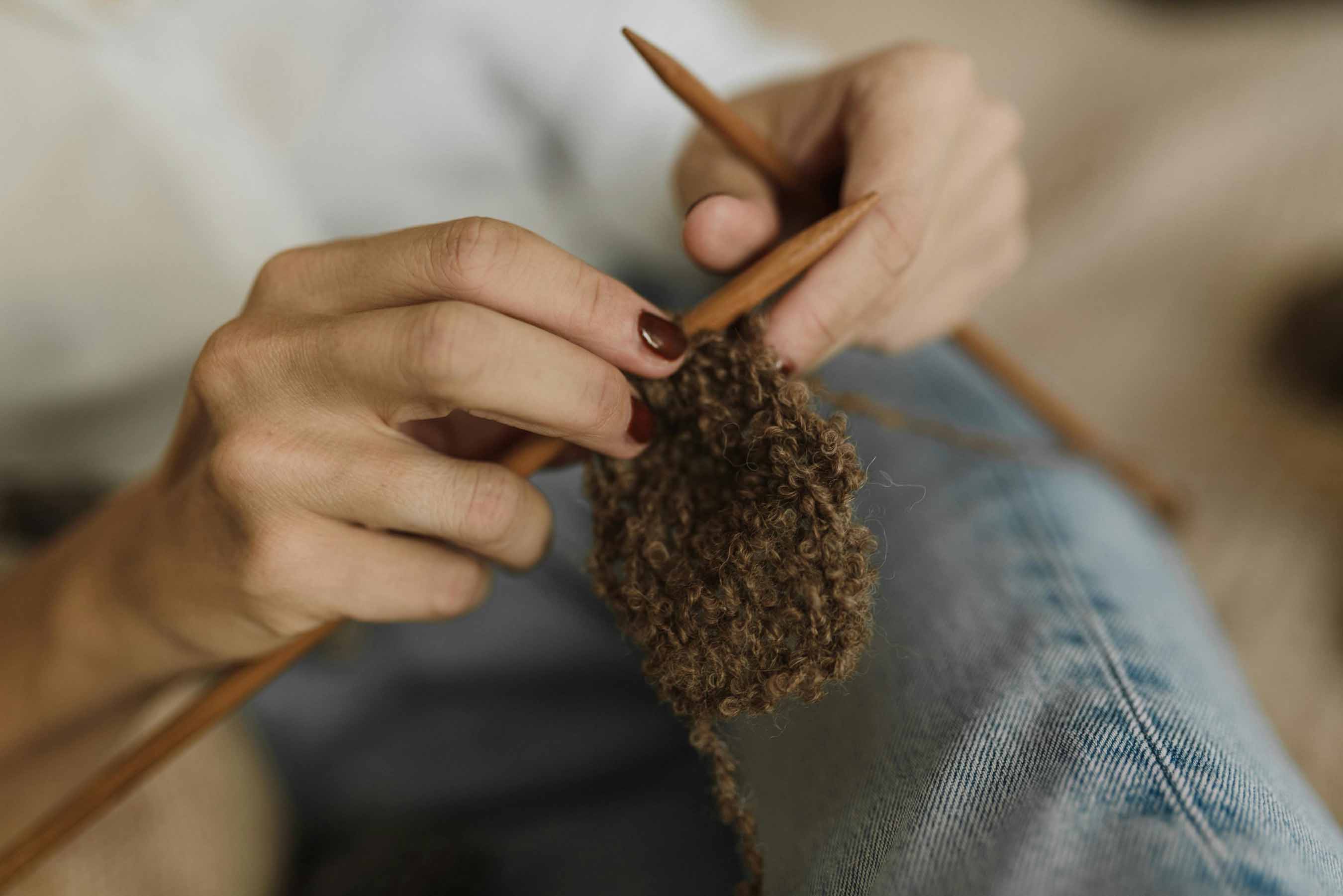 Activité tricot Pays de Gex, gros plan sur des mains maniant des aiguilles et de la laine texturée