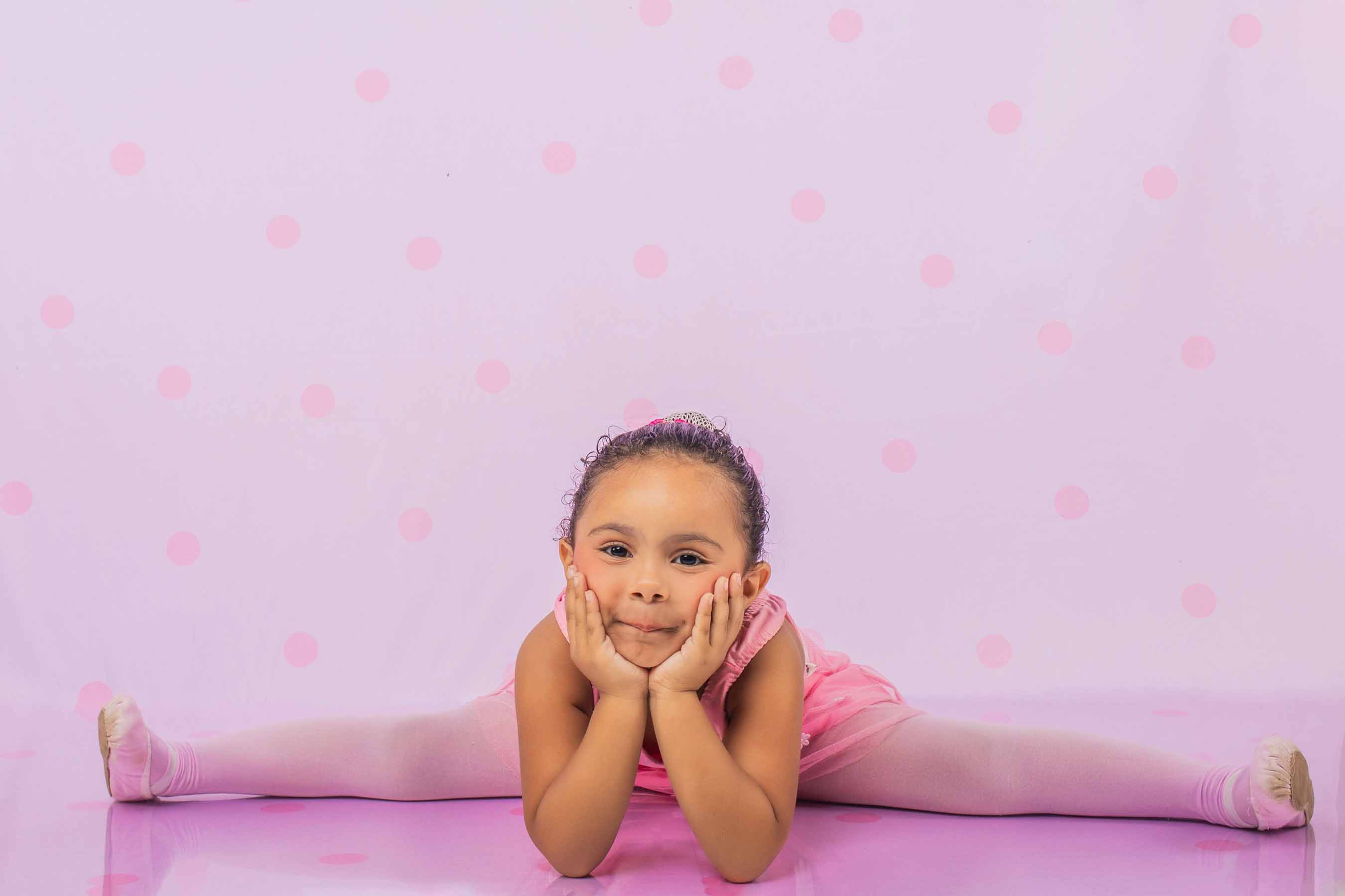 Initiation à la danse et gymnastique, élève souriante réussissant le grand écart facial sur un fond rose à pois