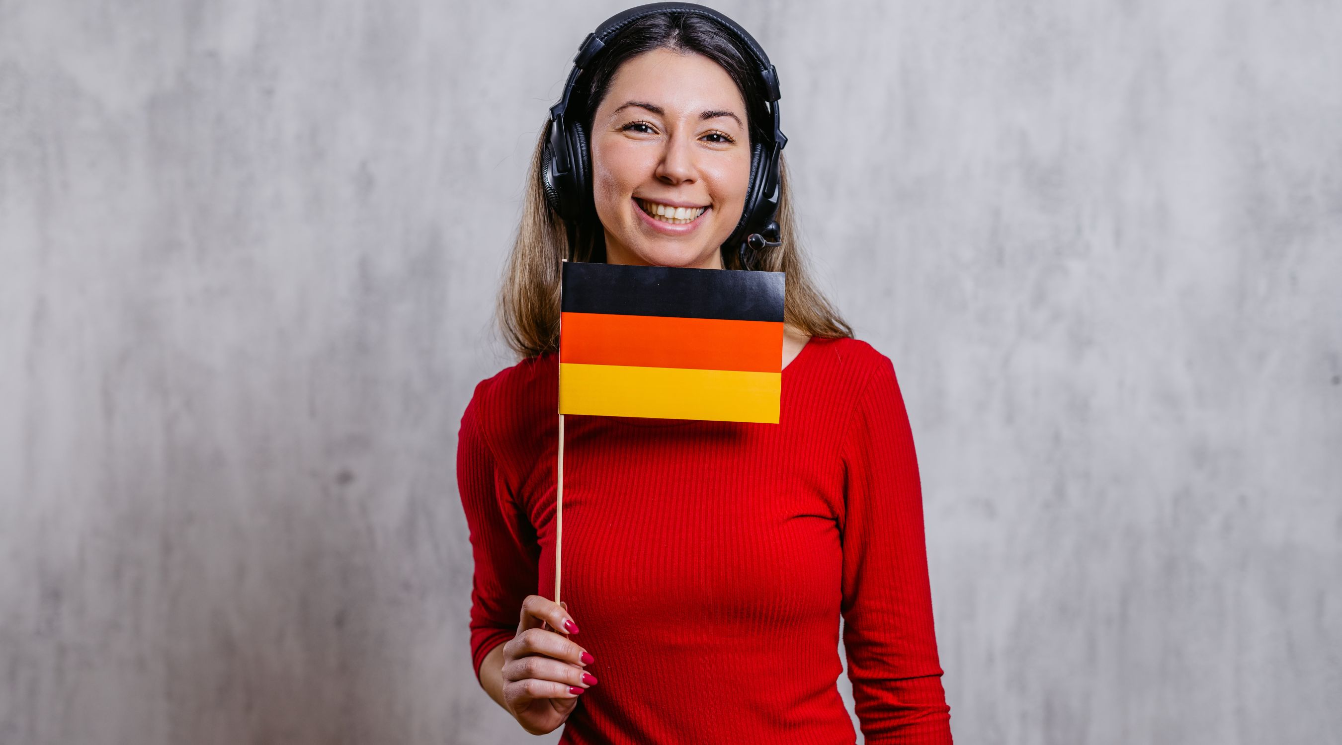 Cours d'allemand, jeune femme souriante avec un casque audio tenant un petit drapeau de l'Allemagne