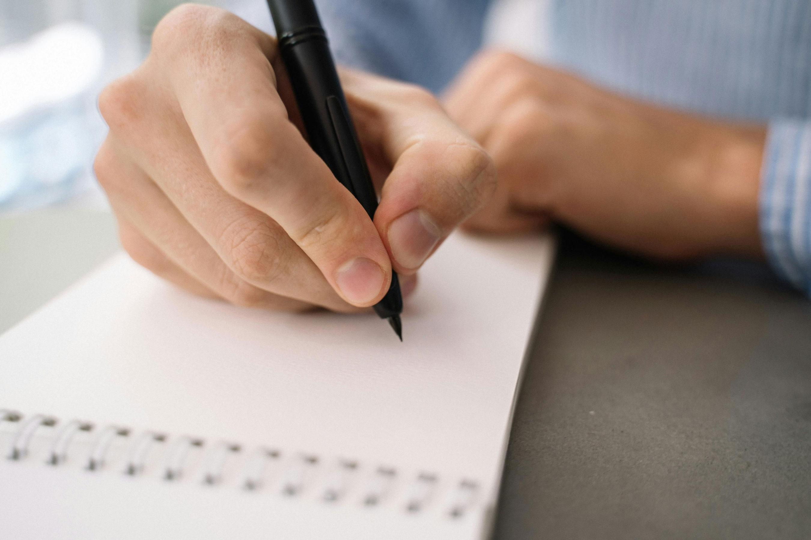 Atelier d'écriture, gros plan sur une main tenant un stylo noir et rédigeant un texte dans un carnet à spirale