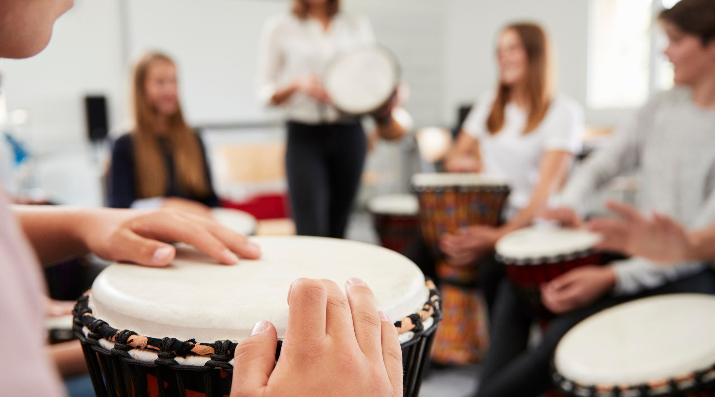 Atelier de percussions, gros plan sur les mains d'un participant jouant du djembé au cœur d'un cercle de musiciens