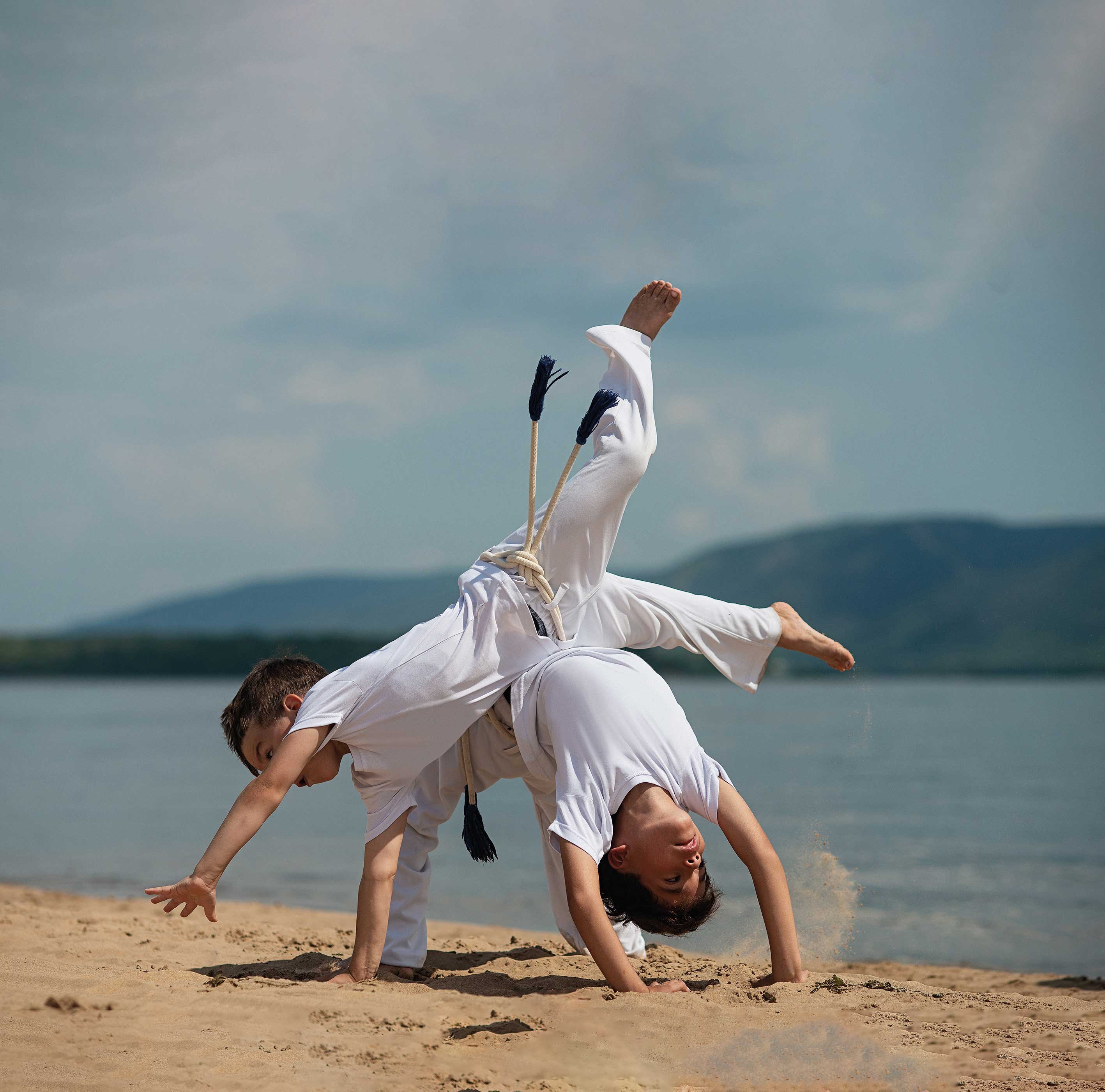 Cours de capoeira, pratiquant en t-shirt rouge réalisant une figure acrobatique en équilibre sur une main devant un mur couvert de graffitis