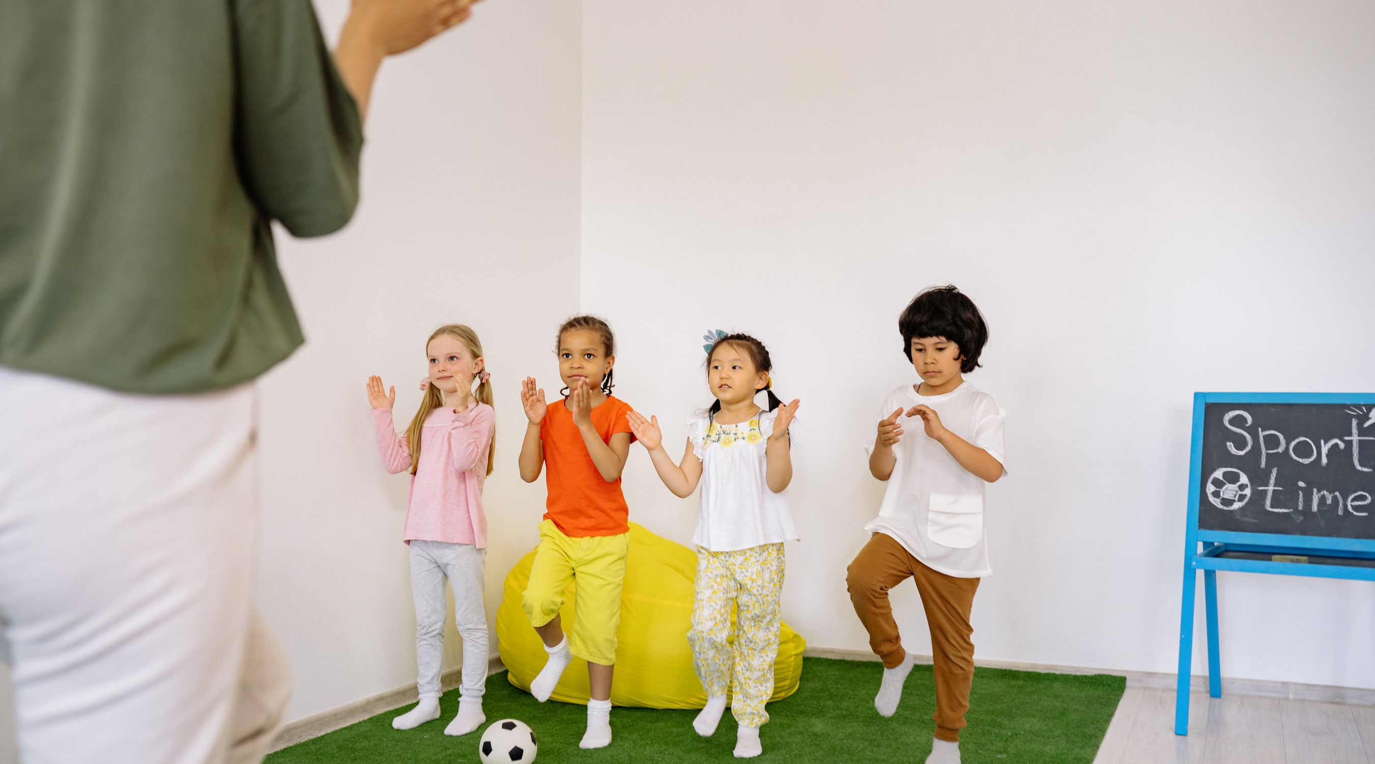 Activité de sport éveil pour les petits, groupe d'enfants imitant les mouvements d'équilibre et de motricité de leur animatrice sur un tapis vert