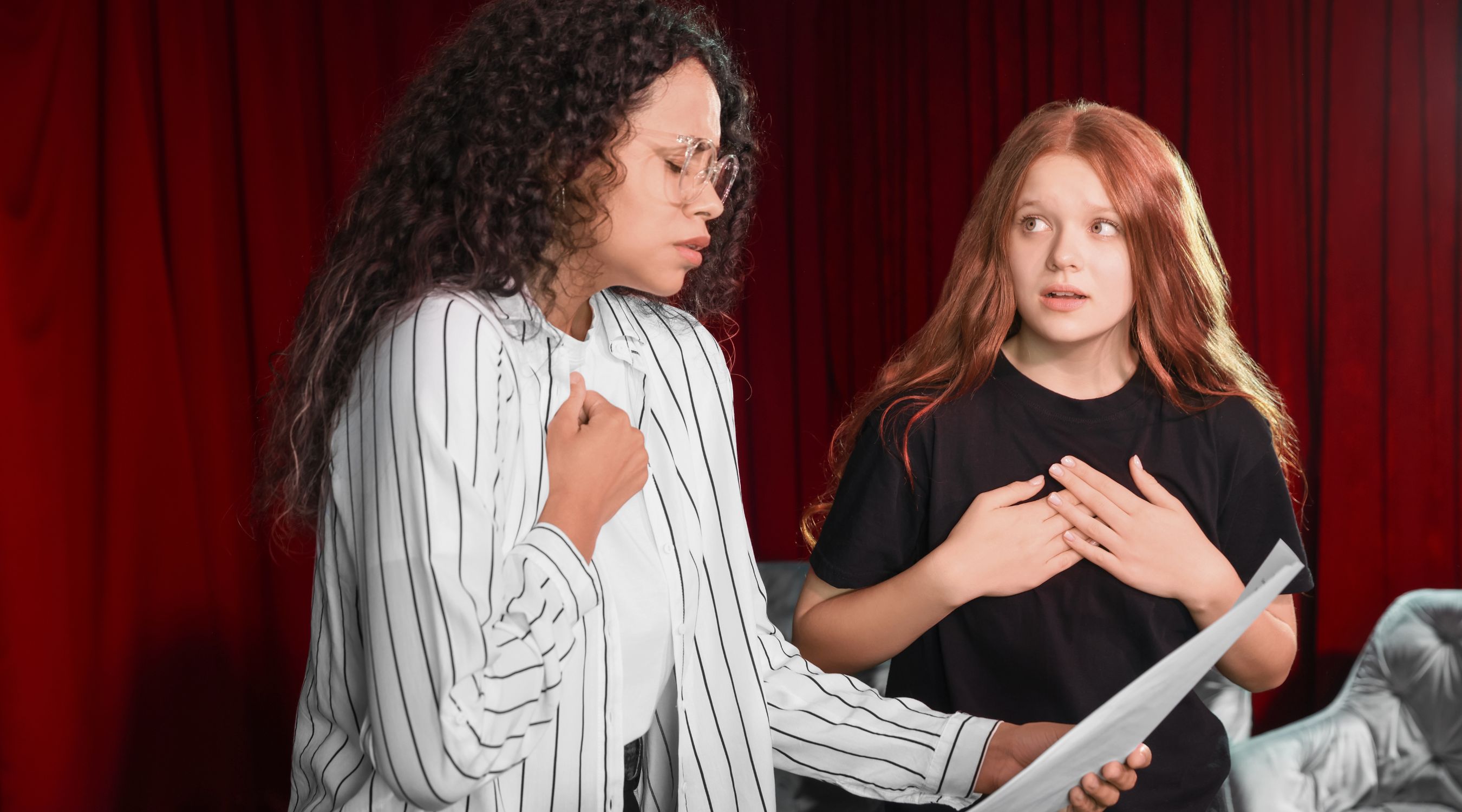 Cours de théâtre à la MJC de Gex, deux comédiennes en pleine répétition jouant une scène d'expression avec un script devant un rideau rouge