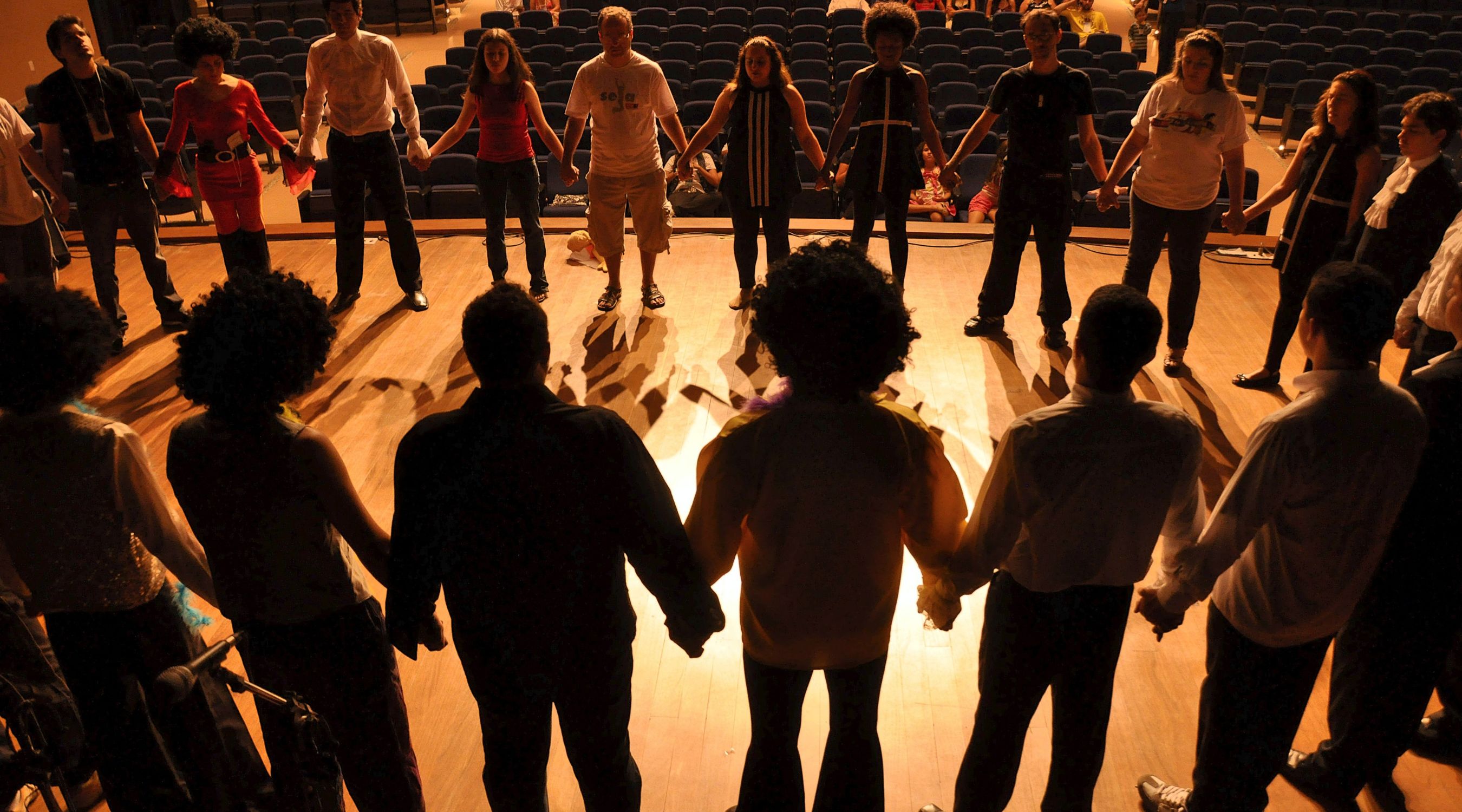 Troupe de théâtre d'improvisation se tenant par la main en grand cercle sur scène sous les projecteurs lors d'un échauffement